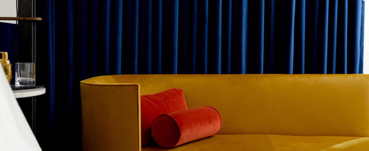 Yellow sofa with red pillows in front of blue drapes at our hotel in Ybor City, FL