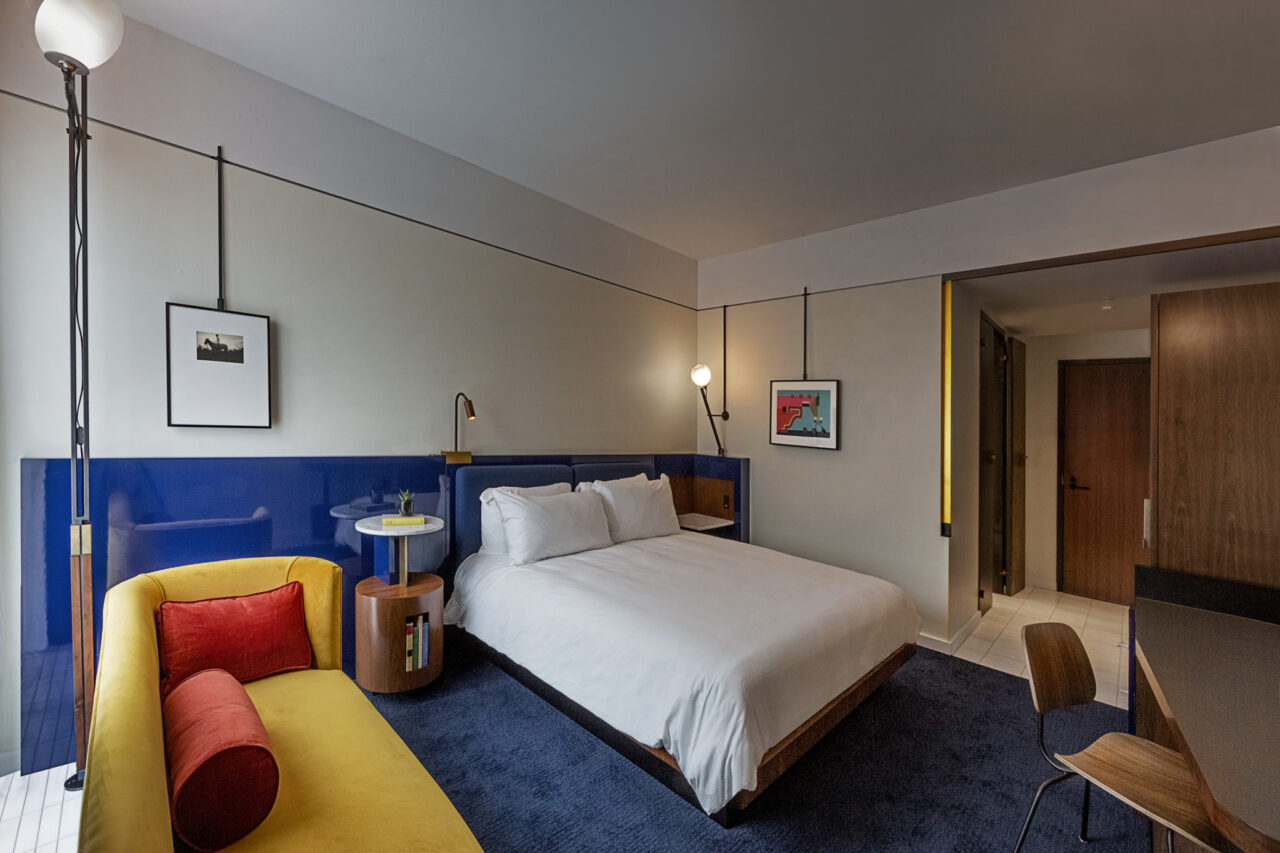 King guestroom with vibrant blue carpet and a yellow sofa with red pillows at our Ybor City Hotel